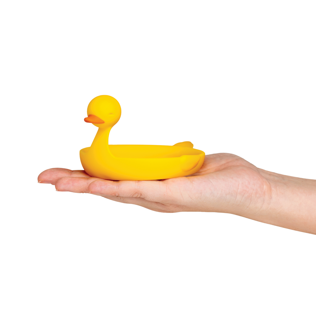 A hand holds the Sunny Side Duck, a small yellow duck-shaped egg separator, against a white background.